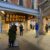 People at a train station looking at an electronic information board displaying train schedules at Bristol Temple Meads, while a few others head towards the ticket barriers.